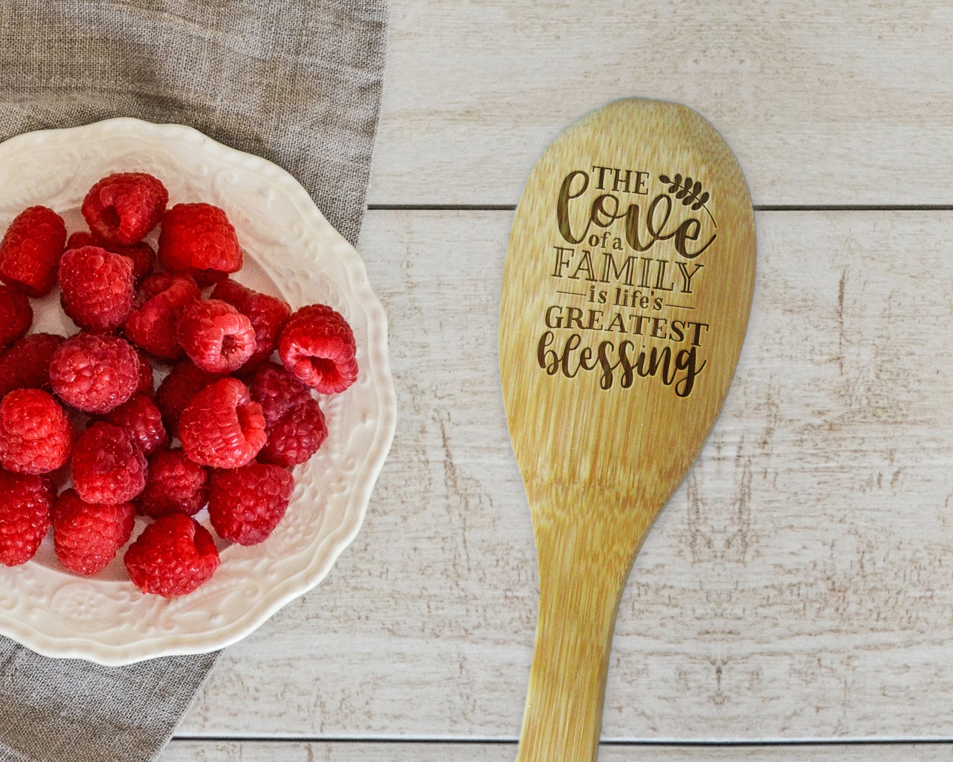 a bowl of raspberries next to a wooden spoon